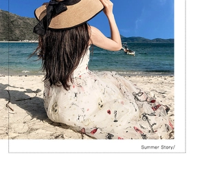 Detail of artistic sun and face embroidery on a white mesh beach dress with straw hat