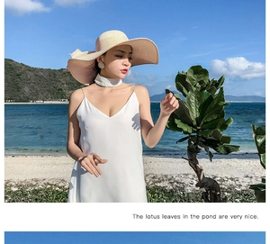 Close-up of wide brim straw sun hat with ribbon bow detail against a beach backdrop