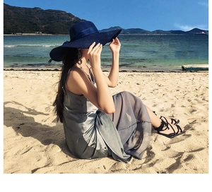 Detail of a navy blue wide brim straw hat paired with a silk maxi dress on a sunny beach