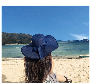 Detail of navy blue wide brim straw hat with elegant bow knot shown in a beach setting