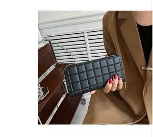 Detail of black quilted long purse with gold zipper held by a fashion model
