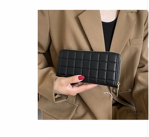 Model holding a black long quilted purse with gold zipper and textured synthetic leather