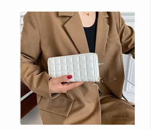 Close-up of white quilted long purse with golden zipper held by a stylish woman