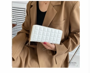 Detailed view of white quilted faux leather long wallet with gold zipper held by model
