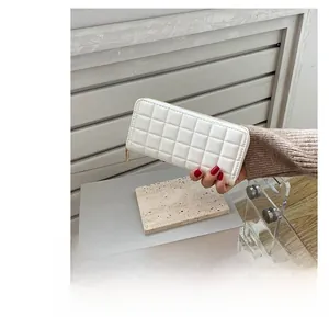 Close-up of white quilted long wallet with golden zipper held against a neutral background