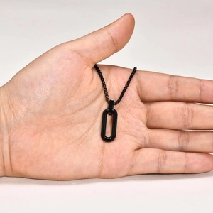 Detail of a minimalist black oval cutout pendant with sleek chain held in hand for scale