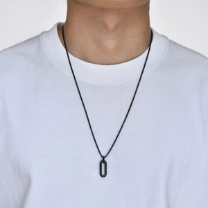Close-up of a men's minimalist black oval pendant necklace worn on a white t-shirt