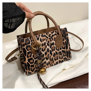 Detail of leopard print crossbody bag with woven bell charm and brown handles