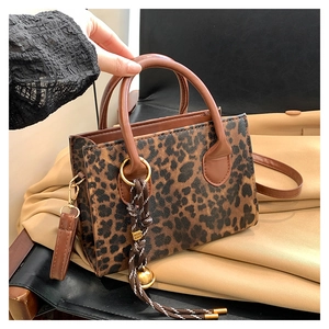 Detail of leopard print handbag with brown leather handles and woven rope tassel