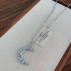 Détail du pendentif lune argenté avec texture lave et zircons sur plateau en lin
