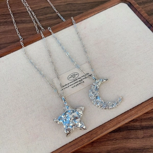 Collier avec pendentifs étoile et lune argentés texturés et zircons sur fond de lin