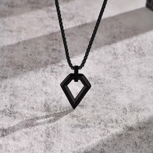 Macro shot of black geometric diamond pendant with industrial box chain on grey marble
