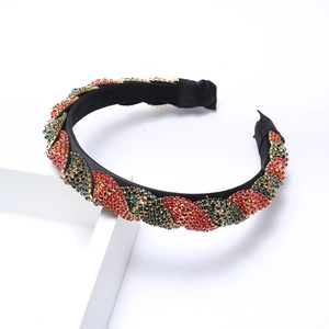 Braided rhinestone headband with red green and gold crystals on a white pedestal
