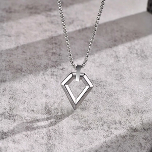 Close-up of geometric hollow rhombus pendant on box chain over grey stone surface
