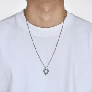 Detail of hollow geometric diamond pendant on a box chain worn over a white T-shirt