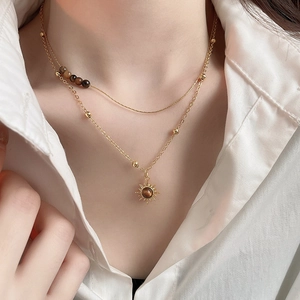 Detail of layered gold sunburst pendant necklace with tiger eye stone on white shirt
