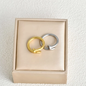 Detail of overlapping gold and silver nail rings on a beige jewelry display box