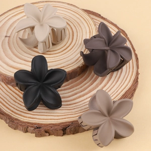 Close-up of four matte frangipani flower hair claws in cream, brown, black and mauve purple