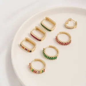 Detail of 14K gold plated huggie earrings with emerald and ruby zircon in white dish