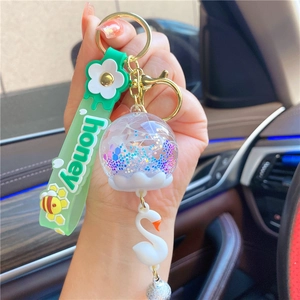 Close-up of a swan liquid bottle keychain with honey silicone strap and bell charm