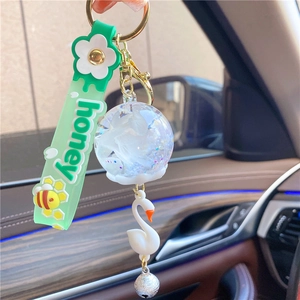 Detail of swan keychain with green honey wristband and glitter filled glass ball