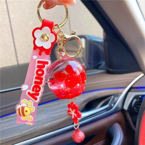 Close-up of a bee-themed glitter bottle keychain with honey wrist strap and red charm