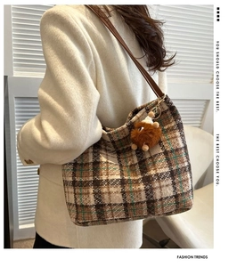 Detailed view of checkered canvas tote bag with brown leather strap and plush charm