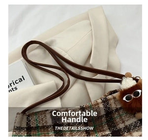 Detail of a brown plaid canvas tote bag featuring a leather strap and plush charm