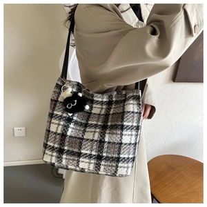 Close-up of checkered tweed tote bag texture with black plush charm and leather strap