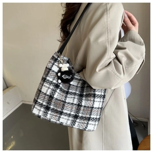 Side view of checkered tweed tote bag with black leather straps and plush monster charm