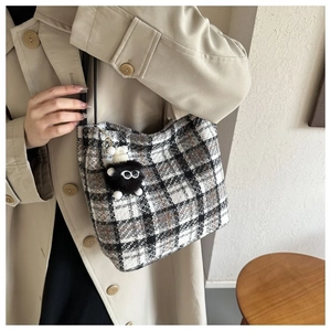 Detail view of plaid tote bag with fuzzy monster charm and long black handles
