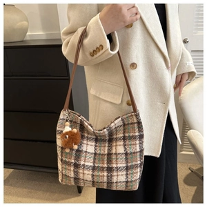 Detail of woven plaid tote bag with brown leather strap and plush animal charm