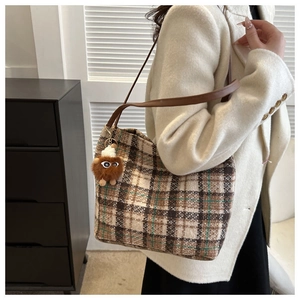 Detail of plaid canvas tote bag featuring brown leather straps and a plush ball charm