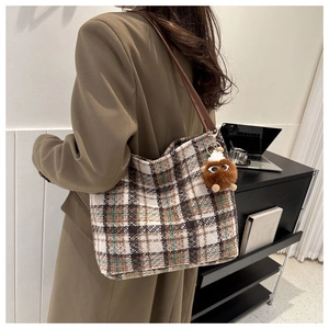 Detail of tweed checkered tote bag with brown leather strap and plush eye pendant