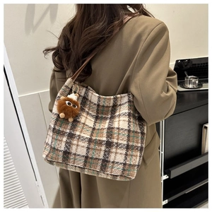 Close-up of plaid tote bag with brown plush pendant shown on model in office setting