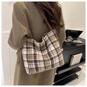 Detail of plaid wool tote bag with brown leather strap in a minimalist office setting