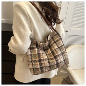 Detail of checkered canvas tote bag with brown straps worn on shoulder by a model