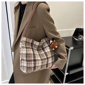 Plaid canvas tote bag with brown leather straps and plush charm worn with dark blazer