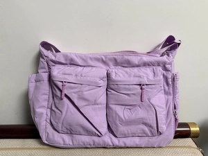 Détail du sac bandoulière en nylon lilas avec deux poches zippées utilitaires sur le devant