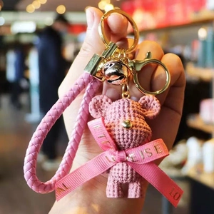 Detail of pink knitted bear keychain with golden bell and braided leather wrist strap