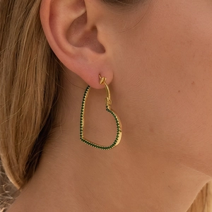 Close-up of golden heart hoop earring with inlaid green zircons worn by model