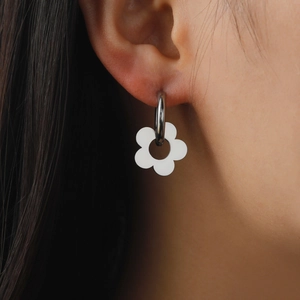 Minimalist silver hoop earrings with a white five-petal flower pendant on female model