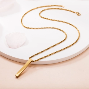 Detailed view of polished gold rectangular bar pendant with slim box chain on stone base