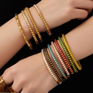 Dettaglio di braccialetti dorati impilati con smalto colorato e strass brillanti