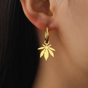 Gold stainless steel hoop earrings featuring a polished maple leaf pendant on a model