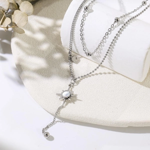 Close-up of double-layer silver chain with mother-of-pearl sunburst pendant on marble stand