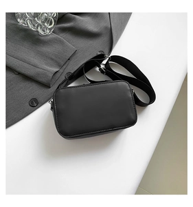 Close-up of minimalist black matte crossbody bag with wide nylon strap on suit background
