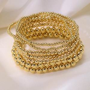 Macro view of layered gold beaded elastic bracelets set on white silk fabric