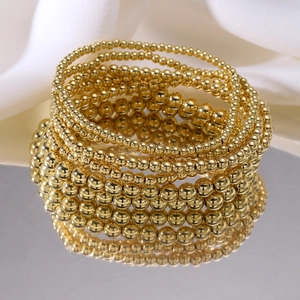 Polished gold beaded stretch bracelet set for women, layered on a reflective silver mirror