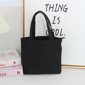 Minimalist black canvas tote bag shown in a cozy indoor home setting with books